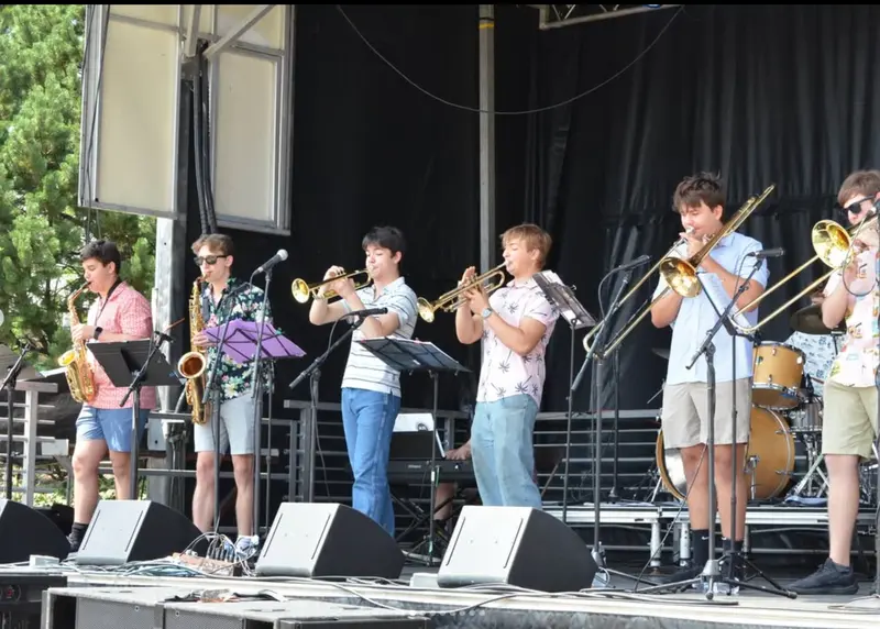 Scholarsjazz saxophones, trumpets, and trombones performing on an outdoor festival stage